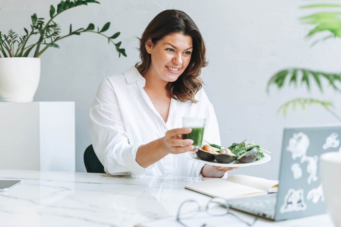 A dietitian holding juice and looking at her computer.